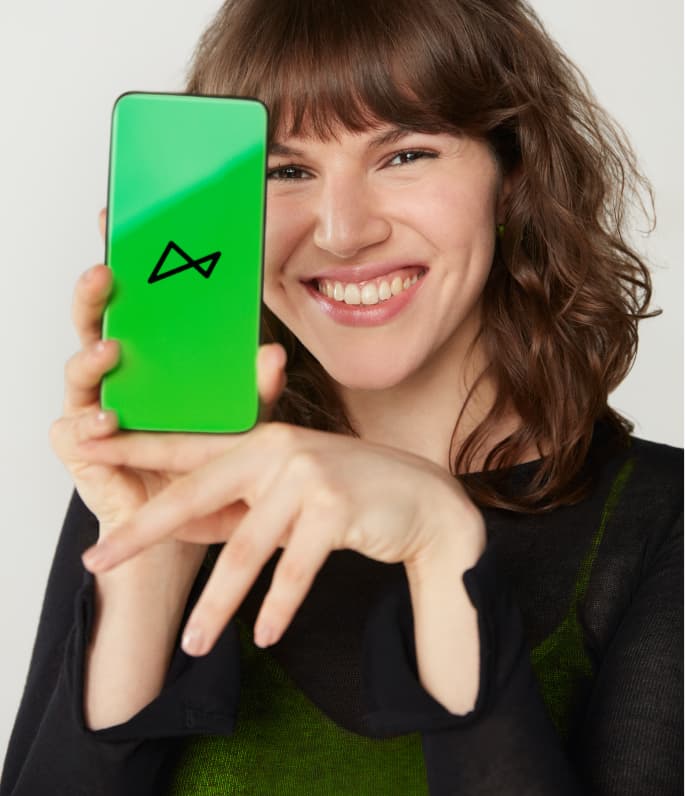 Uma mulher jovem de cabelos castanhos e sorriso grande segura um smartphone com a tela voltada para a frente. Nela, vemos a tela na cor verde mostrando ao meio o logo do next.
