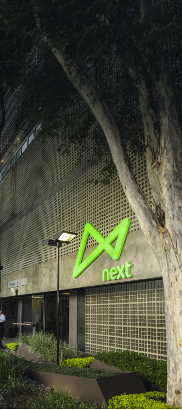 Fotografia da entrada do prédio next mostrando o térreo, com o logo do banco em primeiro plano.